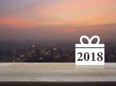 Gift box happy new year 2018 icon on wooden table over blur of cityscape on warm light sundownの写真素材