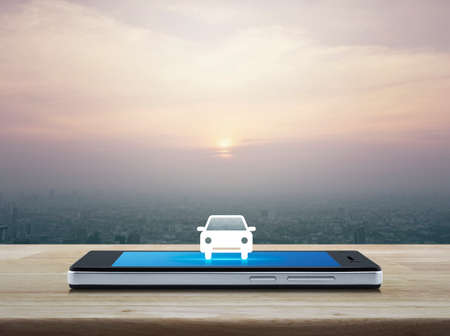 Taxi car flat icon on modern smart phone screen on wooden table over city tower at sunset, vintage style, Business transportation service conceptの写真素材