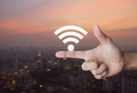 Wifi icon on finger over blur of cityscape on warm light sundown, Technology and internet conceptの写真素材