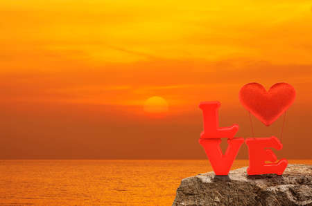 Red love alphabet and fabric heart ballon on rock over sunset sky and sea, Valentines day conceptの写真素材