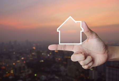 House icon with copy space on finger over blur of cityscape on warm light sundown, Real estate conceptの写真素材