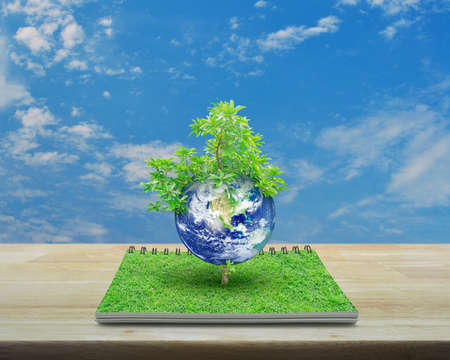 Earth with tree from an open book on wooden table over blue sky with white clouds, Ecology concept, Elements of this image furnishedの写真素材