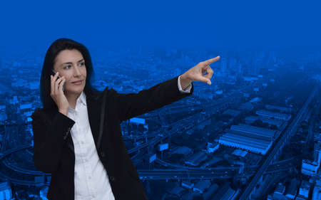 Caucasian business woman talking on her cell phone and pointing or touching touchscreen over modern city tower, street and expressway, Business communication conceptの写真素材