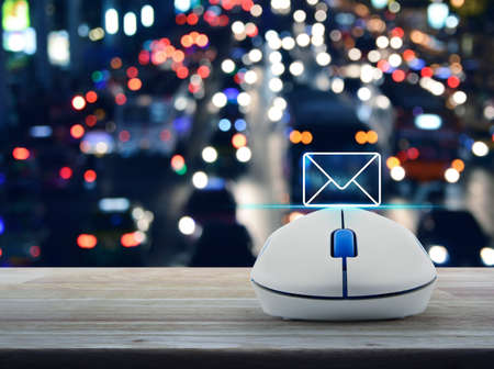 Mail flat icon with wireless computer mouse on wooden table over blurred colourful night light city with cars, Contact us conceptの写真素材
