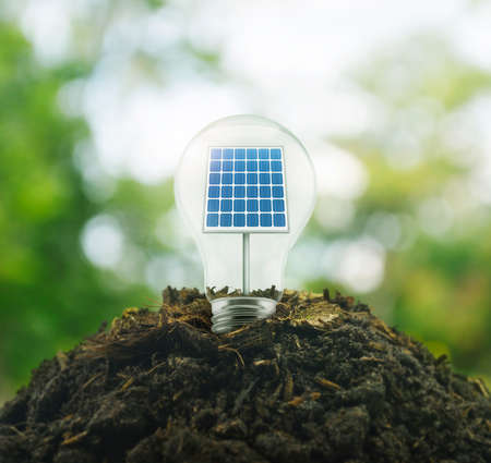 Light bulb with solar cell inside on pile of soil over green environment, Ecological conceptの写真素材
