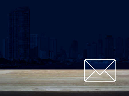Mail icon on wooden table over modern office city tower background, Contact us conceptの写真素材