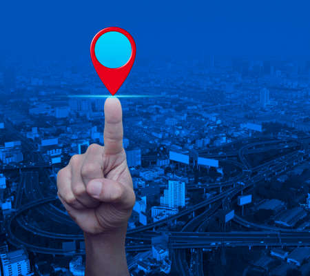 Businessman pressing map pin location button over modern city tower, street and expressway, Map pointer navigation conceptの写真素材