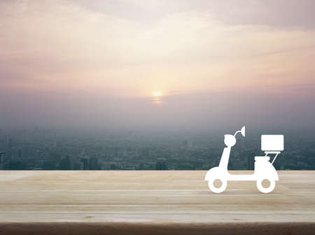 Motor bike icon on wooden table over city tower at sunset, vintage style, Business delivery service conceptの写真素材