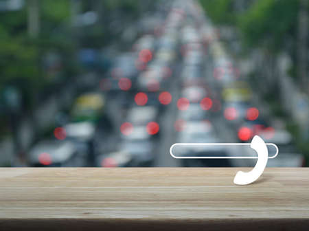 Phone icon with copy space for add your phone number on wooden table over blur of rush hour with cars and road, Contact us conceptの写真素材