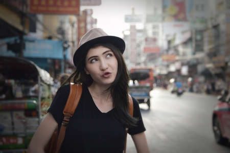 Young asian happy woman traveler with a backpack on her shoulder and travel hat standing over China town, Bangkok, Thailand, Travel holiday relaxation conceptの写真素材