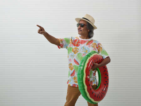 Happy elderly traveler asian man wearing summer t-shirt, straw hat and sunglasses, pointing finger...