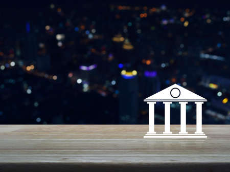 Bank icon on wooden table over blur colorful night light of modern city tower and skyscraper, Business banking online conceptの写真素材