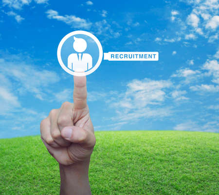 Hand pressing businessman with magnifying glass icon over green grass field with blue sky and white clouds, Business recruitment online conceptの写真素材