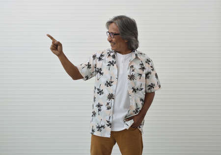 Happy senior traveler asian man wearing glasses, summer shirt and brown shorts and pointing finger...