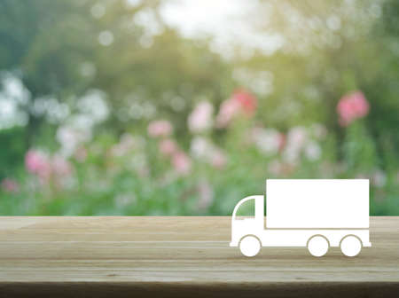 Truck flat icon on wooden table over blur pink flower and tree, Business transportation service online conceptの写真素材