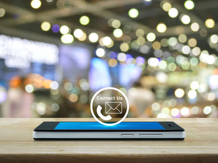 Telephone and email icon button on modern smart mobile phone screen on wooden table over blur light...