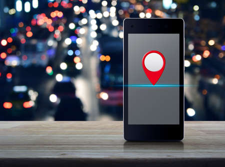 Map pin location button on modern smart mobile phone screen on wooden table over blur colorful night...