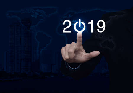 Businessman pressing 2019 start up business icon over world map and modern city tower, Happy new year conceptの写真素材