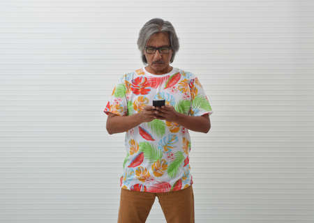 Serious elderly traveler asian man wearing summer t-shirt and glasses looking at smart mobile phone...