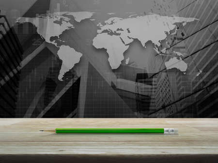Green pencil on wooden table over world map with financial graph and modern city tower, Business concept and ideaの写真素材
