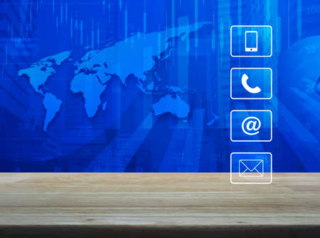 Telephone, mobile phone, www and email buttons on wooden table over world map with financial graph and modern city tower, Business customer support conceptの写真素材