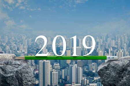 2019 white text with green pencil on rock mountain over modern city tower, office building and...