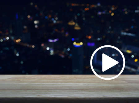 Play button flat icon on wooden table over blur colorful night light city tower and skyscraper, Business music online conceptの写真素材
