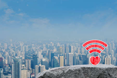 Red heart love wifi flat icon on rock mountain over modern city tower, office building and...