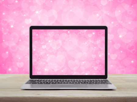 Modern laptop computer with love heart screen on wooden table over pink background, Business internet dating online, Valentines day conceptの写真素材