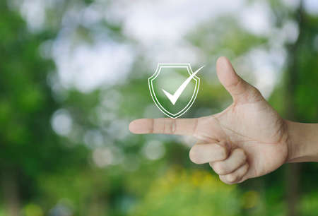 Security shield with check mark icon on finger over blur green tree in park, Technology internet...