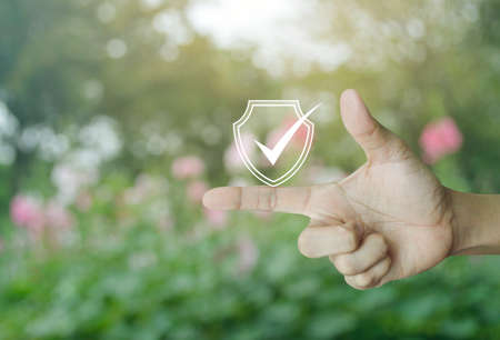 Security shield with check mark icon on finger over blur pink flower and tree in park, Technology internet cyber security and anti virus conceptの写真素材