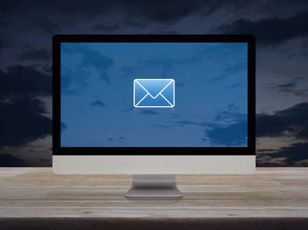 email flat icon on desktop modern computer monitor screen on wooden table over sunset sky, Business contact us online conceptの写真素材