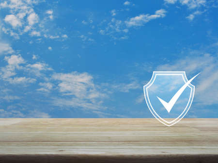 Security shield with check mark flat icon on wooden table over blue sky with white clouds,...
