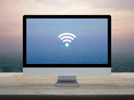 Wifi flat icon on desktop modern computer monitor screen on wooden table over city tower and skyscraper at sunset sky, vintage style, Technology and internet conceptの写真素材