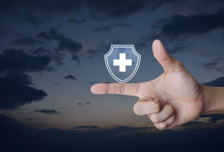 Cross shape with shield flat icon on finger over sunset sky, Business healthy and medical care insurance conceptの写真素材
