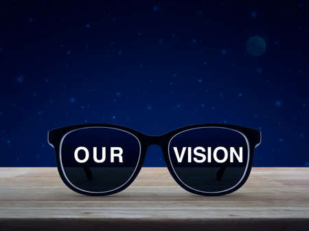 Black glasses with our vision text on wooden table over fantasy night sky and moonの写真素材