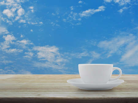 White coffee cup on wooden table over blue sky with white cloudsの写真素材