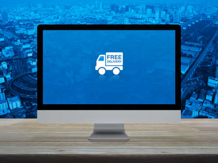 Free delivery truck flat icon on desktop modern computer monitor screen on wooden table over city...