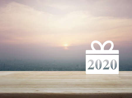 Gift box happy new year 2020 flat icon on wooden table over modern city tower and skyscraper at sunset, vintage style, Business shop online conceptの写真素材