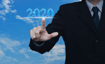 Businessman pressing 2020 text over blue sky with white clouds, Happy new year 2020 calendar cover conceptの写真素材