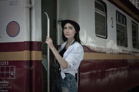 Happy young beautiful woman traveler holding camera and travel map standing on stairs vintage train,...