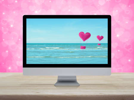 Pink fabric heart love air balloon on tropical sea with desktop modern computer monitor screen on wooden table over blur pink background, Business internet dating online, Valentines day conceptの写真素材