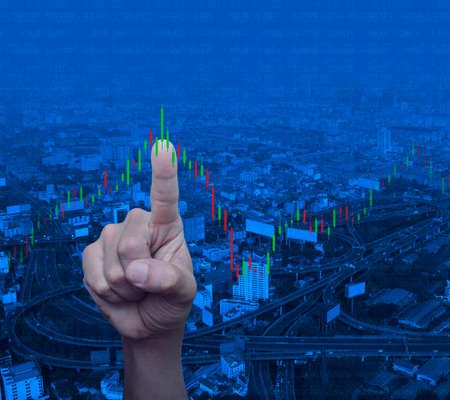 Hand pressing to trading graph of stock market over modern city tower, street, expressway and skyscraper, Business investment conceptの写真素材