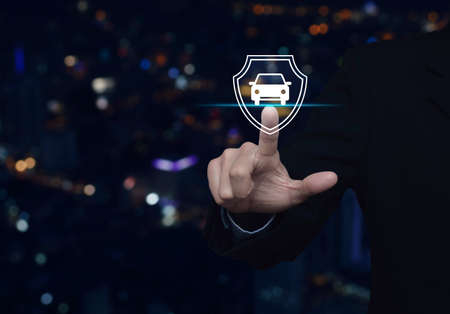 Businessman pressing car with shield flat icon over blur colorful night light city tower and skyscraper, Business automobile insurance conceptの写真素材