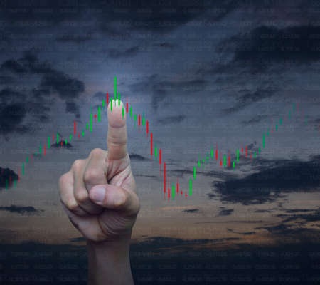 Hand pressing to trading graph of stock market over sunset sky, Business investment conceptの写真素材