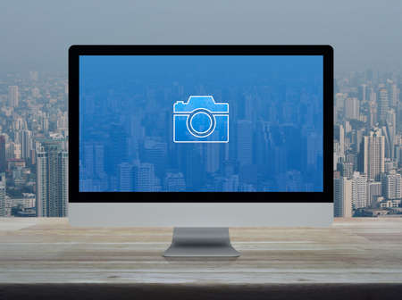Camera flat icon with modern laptop computer on wooden table over office building tower and skyscraper in city, Business camera service shop online conceptの写真素材