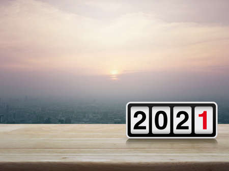 Retro flip clock with 2021 text on wooden table over modern city tower and skyscraper at sunset, vintage style, Happy new year 2021 cover conceptの写真素材