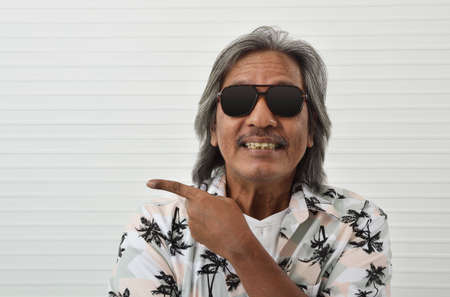 Portrait of happy senior traveler asian man wearing sunglasses and summer shirt pointing finger up...