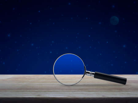 Magnifying glass on wooden table over fantasy night sky and moon, Business analyzing conceptの写真素材
