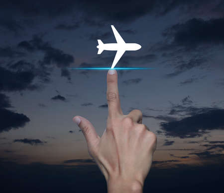 Hand pressing airplane flat icon over sunset sky, Business transportation conceptの写真素材